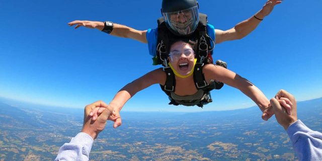 Tandem skydiving student in freefall holding hands of outside videographer at PNW Skydiving in Oregon