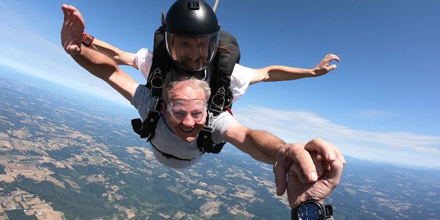 older gentleman smiles in freefall while grabbing camera flyers hand