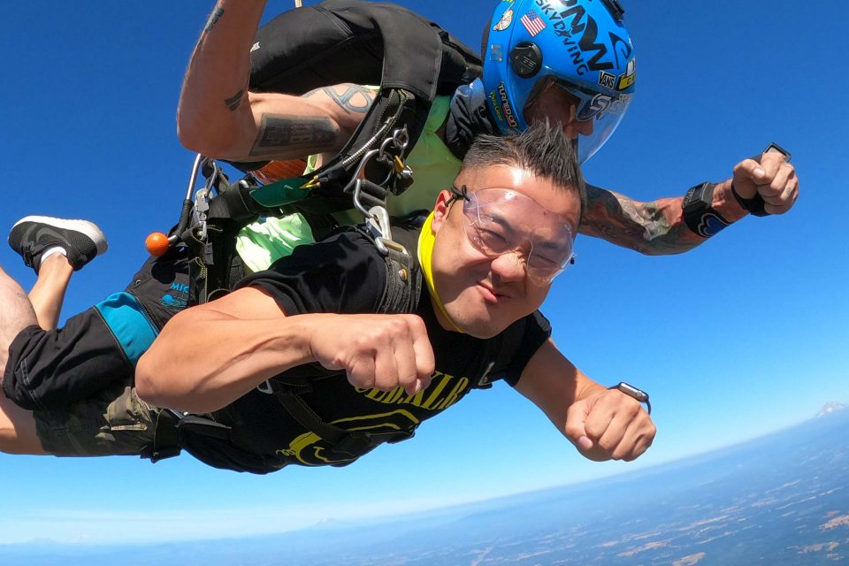 Tandem skydiving student in freefall giving fist bump